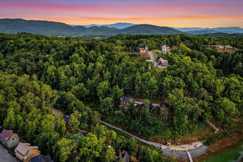 Aerial view capturing the property nestled among lush forests with mountain ridges stretching across the horizon at dusk, showcasing the scenic natural surroundings and secluded setting of the area.
