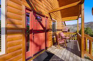 Charming log cabin entrance with rustic porch and mountain views welcomes guests to a peaceful retreat.