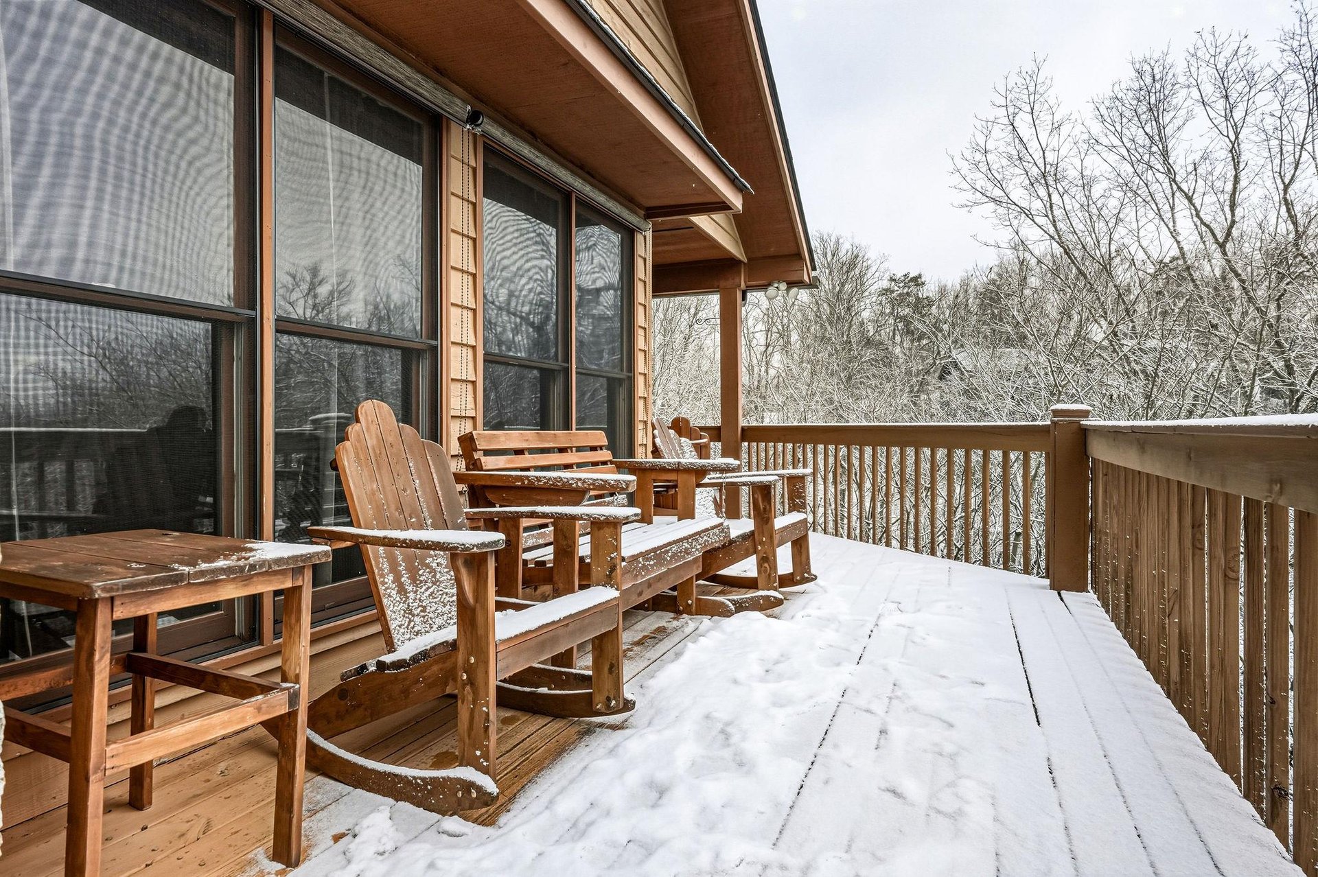 Snowdusted deck with wooden chairs overlooking peaceful winter woods  perfect for cozy mornings with hot cocoa.