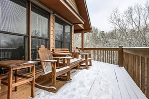 Snowdusted deck with wooden chairs overlooking peaceful winter woods  perfect for cozy mornings with hot cocoa.