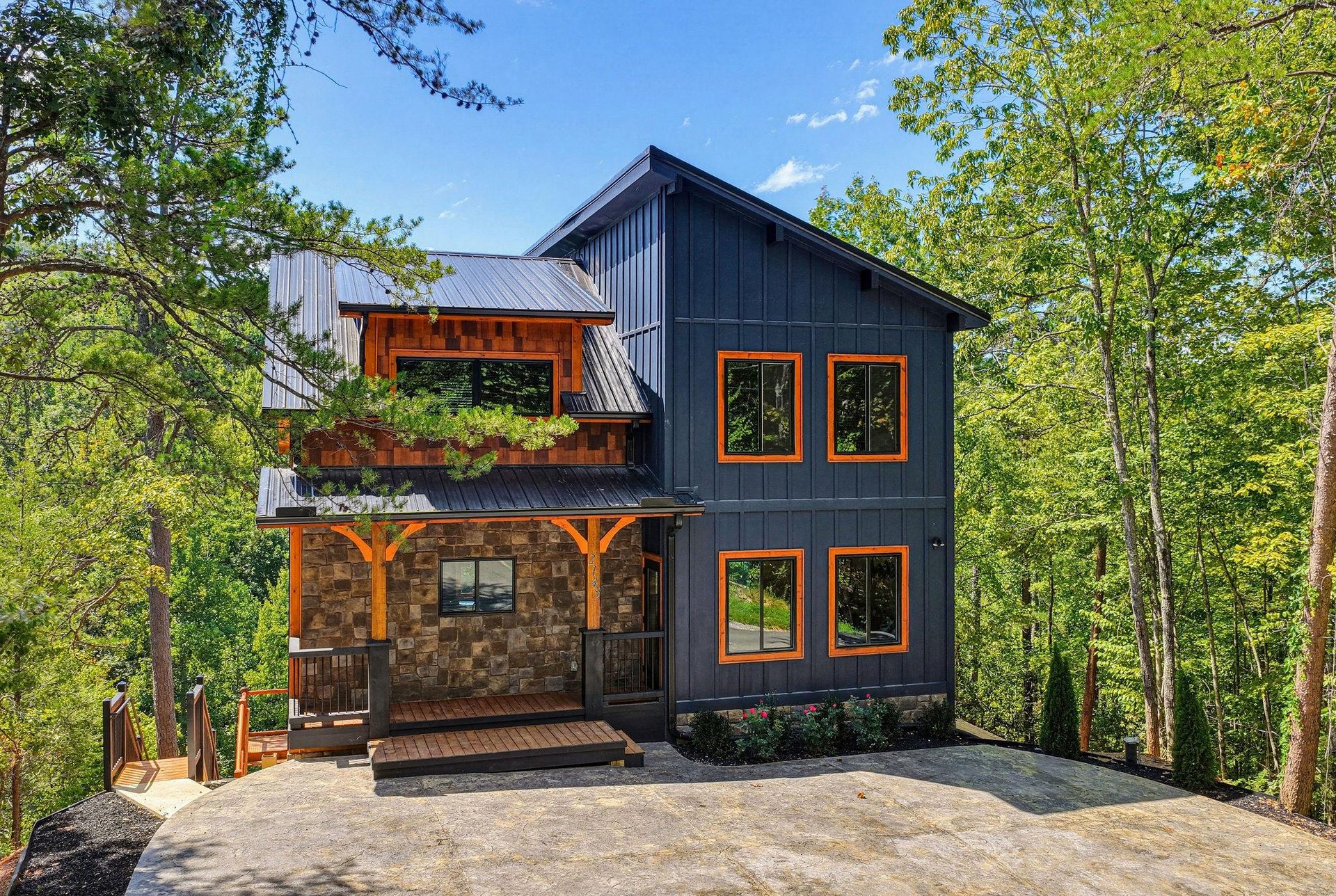 A striking modern mountain retreat with charcoal siding and warm wood accents, nestled privately among towering trees with covered decks perfect for morning coffee.