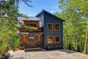 A striking modern mountain retreat with charcoal siding and warm wood accents, nestled privately among towering trees with covered decks perfect for morning coffee.