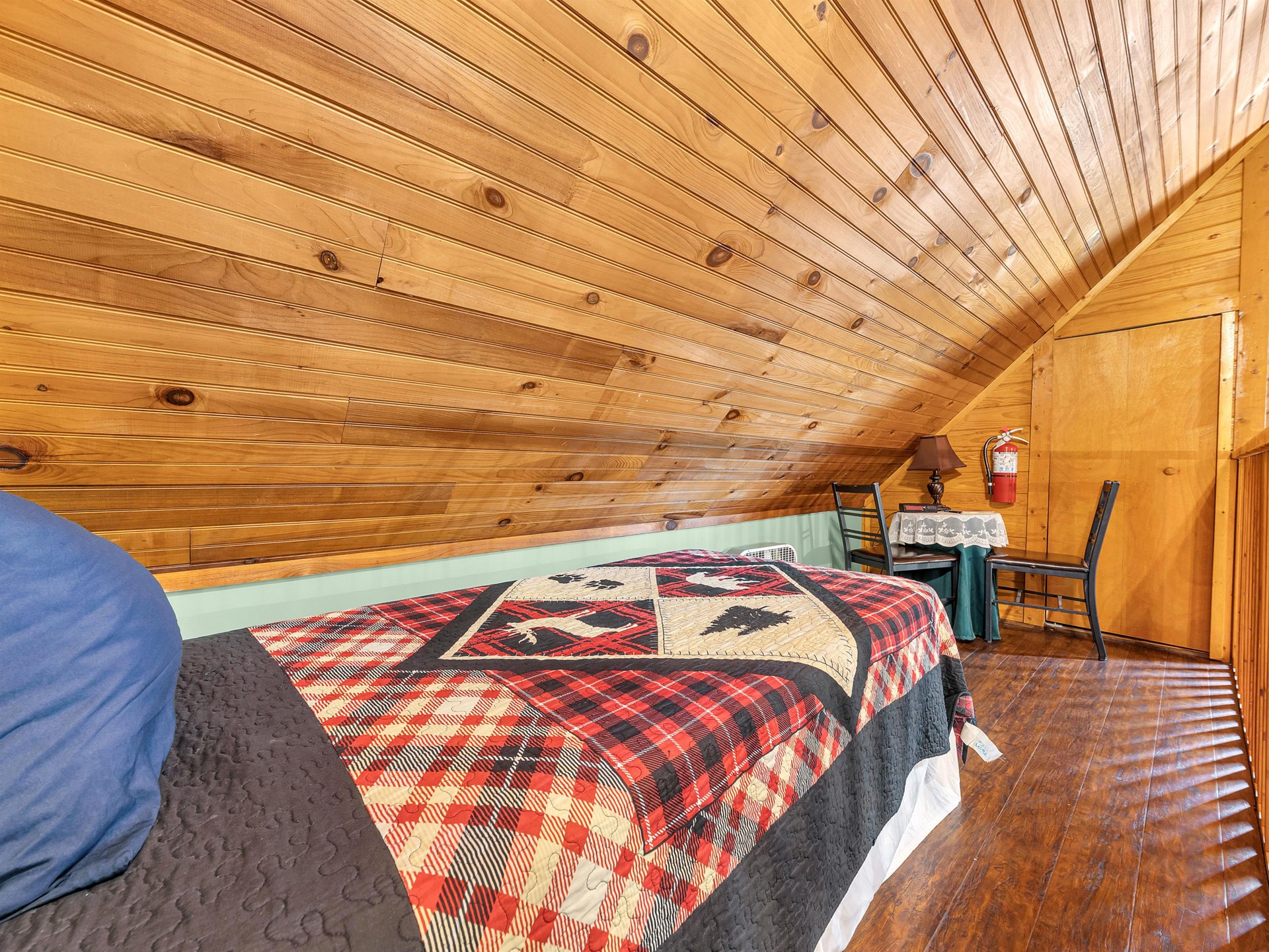 Cozy up in this charming loft bedroom where wood beams create warmth overhead and plaid quilts invite restful nights.