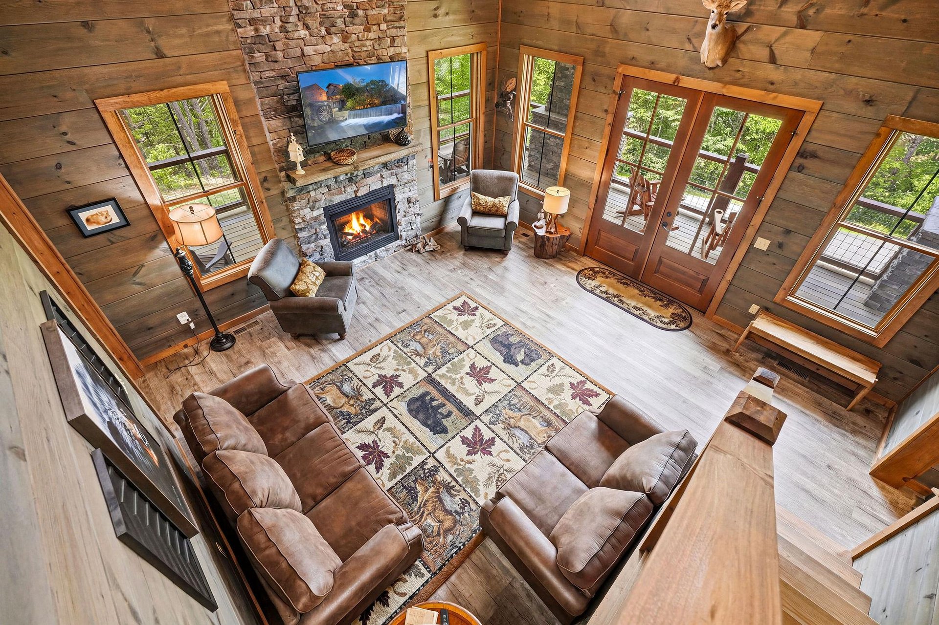 Step into this stunning great room where rustic charm meets modern comfort. Warm up by the stone fireplace, sink into plush seating, and soak in forest views through floortoceiling windows that floo