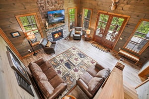 Step into this stunning great room where rustic charm meets modern comfort. Warm up by the stone fireplace, sink into plush seating, and soak in forest views through floortoceiling windows that floo