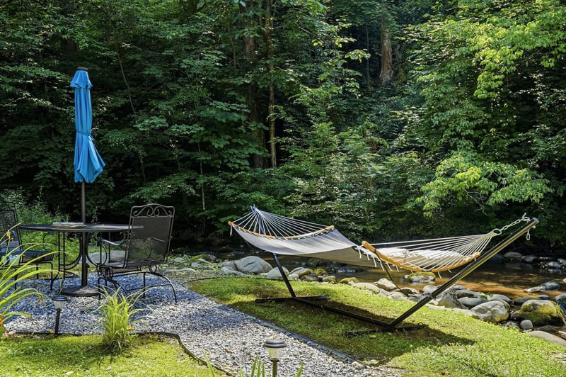 A serene outdoor retreat where a hammock overlooks a peaceful forest stream, perfect for your morning coffee or afternoon nap surrounded by natures calming sounds.