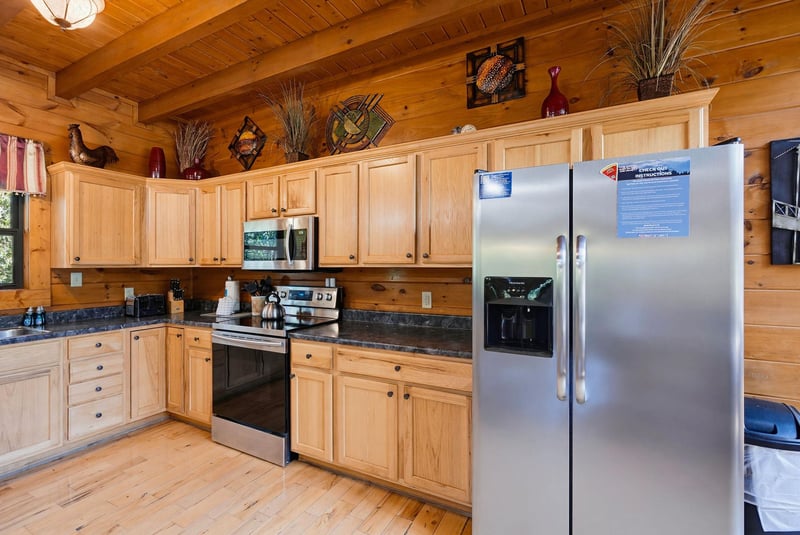Your rustic cabin kitchen blends warm wood tones with modern convenience—spacious counters, full appliances, and charming decor invite you to cook and gather comfortably.