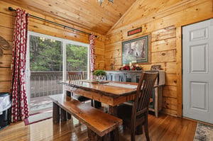Step into a warm cabin retreat where rustic charm meets comfort. Your meals are served at a handcrafted liveedge table, surrounded by knotty pine and views of lush greenery beyond the deck.