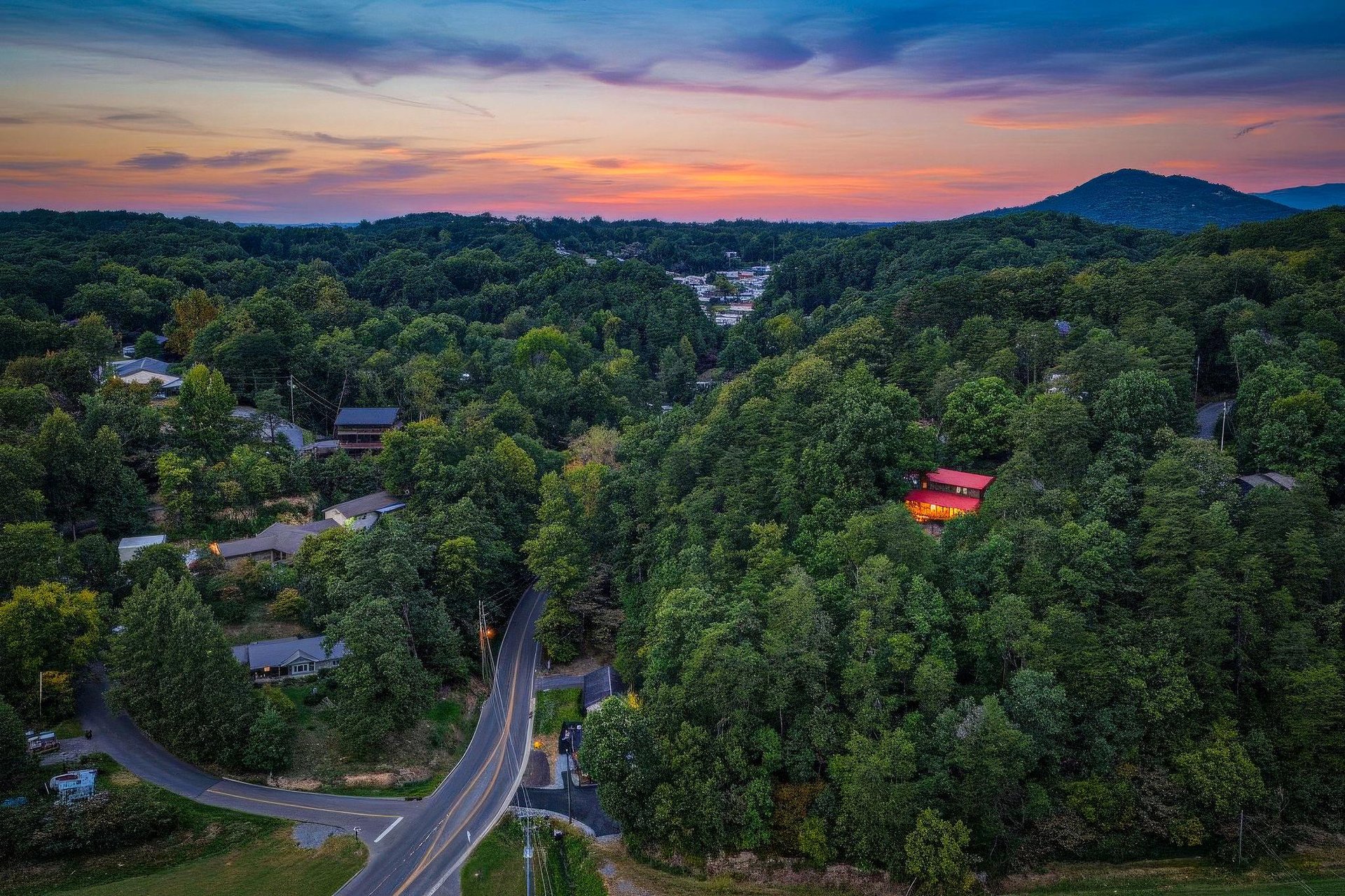 Aerial view captures the property nestled among forested mountains at sunset, with winding roads leading to this peaceful mountain retreat.