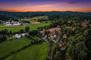 Aerial view at sunset showing the property nestled among rolling hills and lush greenery, with charming cabins and facilities surrounded by a peaceful rural landscape.