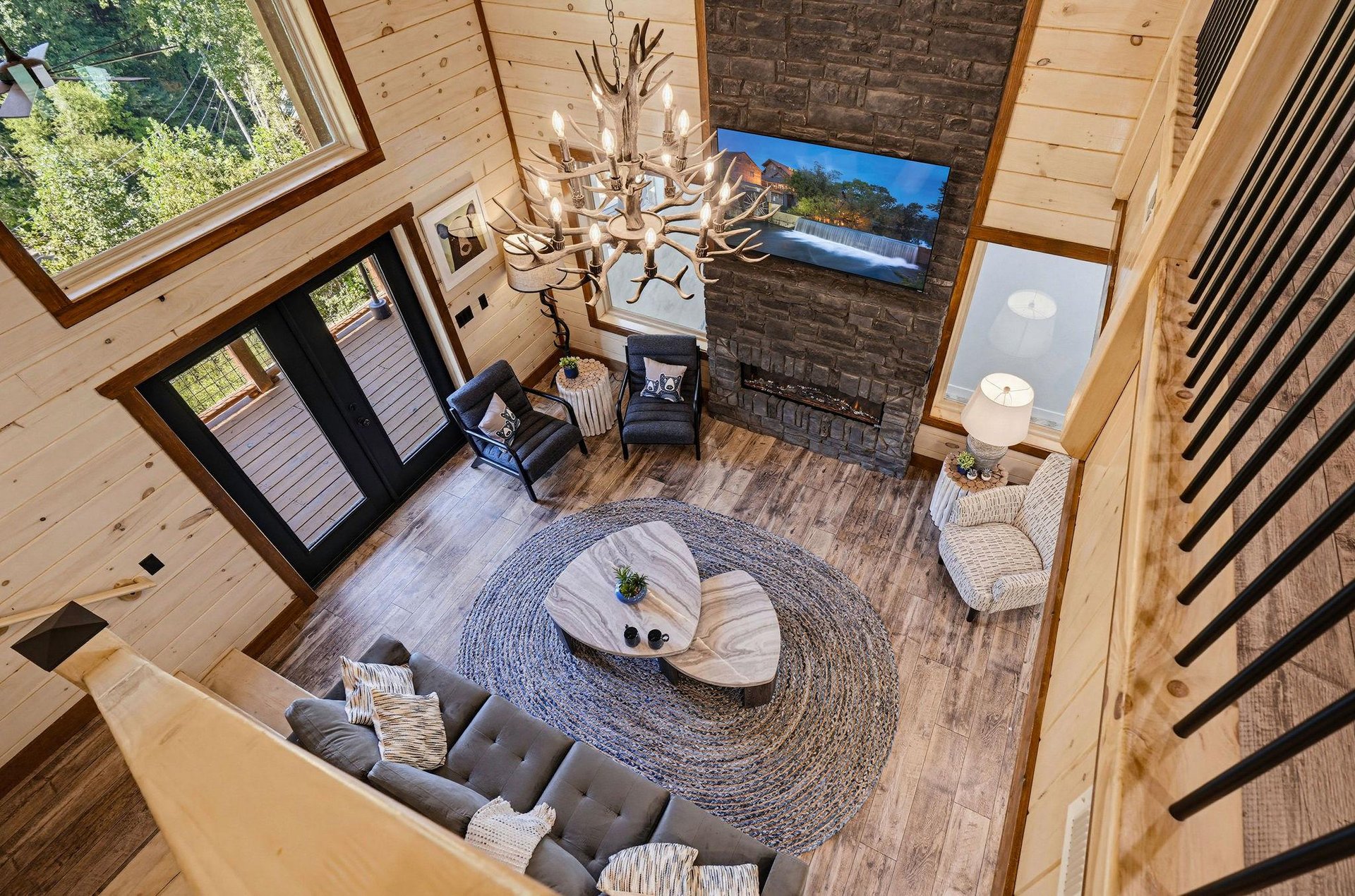 Relax in this stunning vaulted living room, where warm wood tones, a grand antler chandelier, and cozy seating invite you to unwind. The stone fireplace and soaring windows create a perfect mountain r