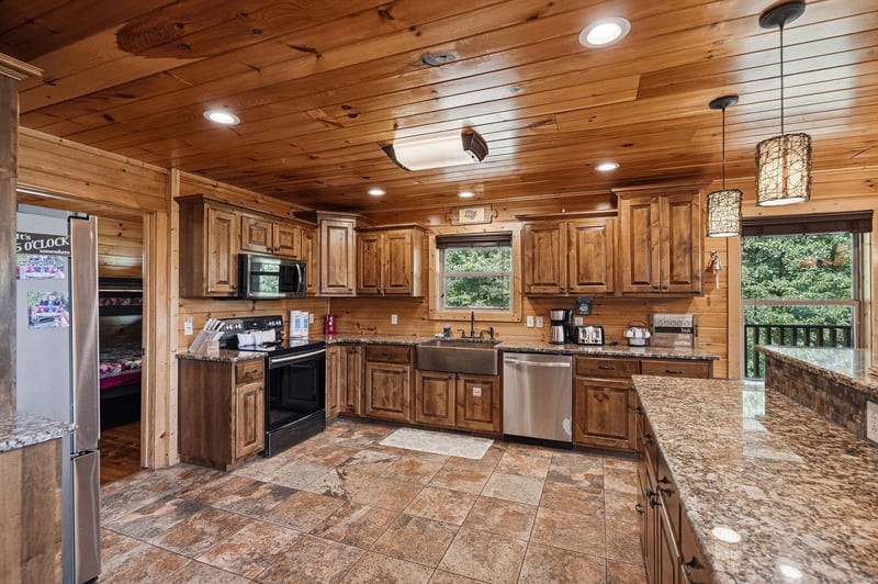 Your spacious gourmet kitchen features warm wood cabinetry, granite countertops, stainless appliances, and a farmhouse sink—perfect for preparing meals while enjoying views of lush greenery through ex