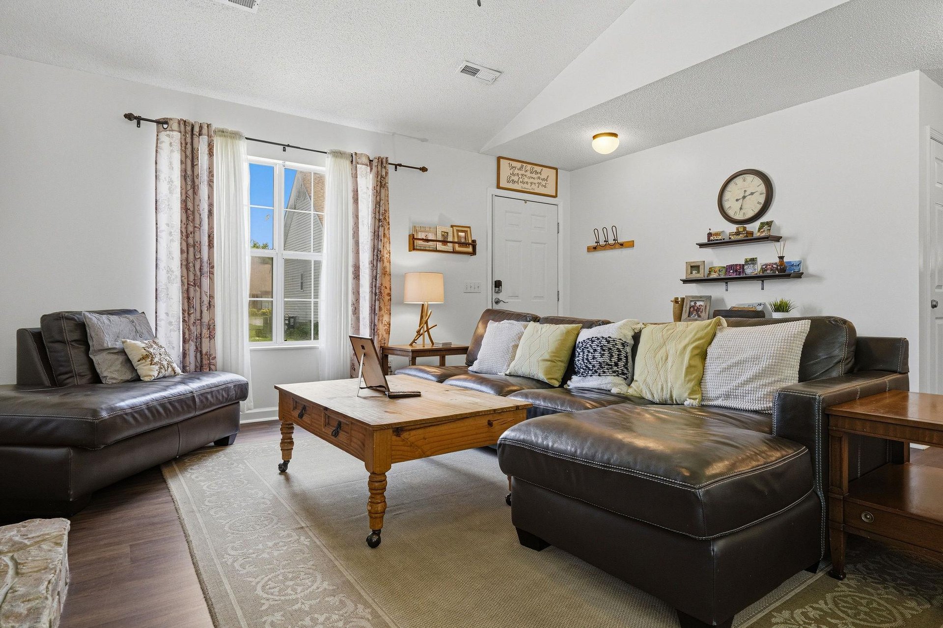 Unwind in your spacious living room with plush leather seating and natural light streaming through large windows. The warm wood accents and thoughtful decor create an inviting space for relaxation.
