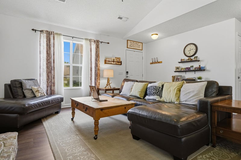 Unwind in your spacious living room with plush leather seating and natural light streaming through large windows. The warm wood accents and thoughtful decor create an inviting space for relaxation.