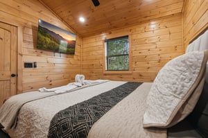 Your cozy cabin bedroom wraps you in warm wood walls, where soft linens and mountain views on the TV create your perfect retreat.