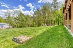 An expansive lawn bordered by mature spring trees creates a peaceful natural setting. The open yard offers generous space for outdoor activities or simply unwinding in the fresh air.