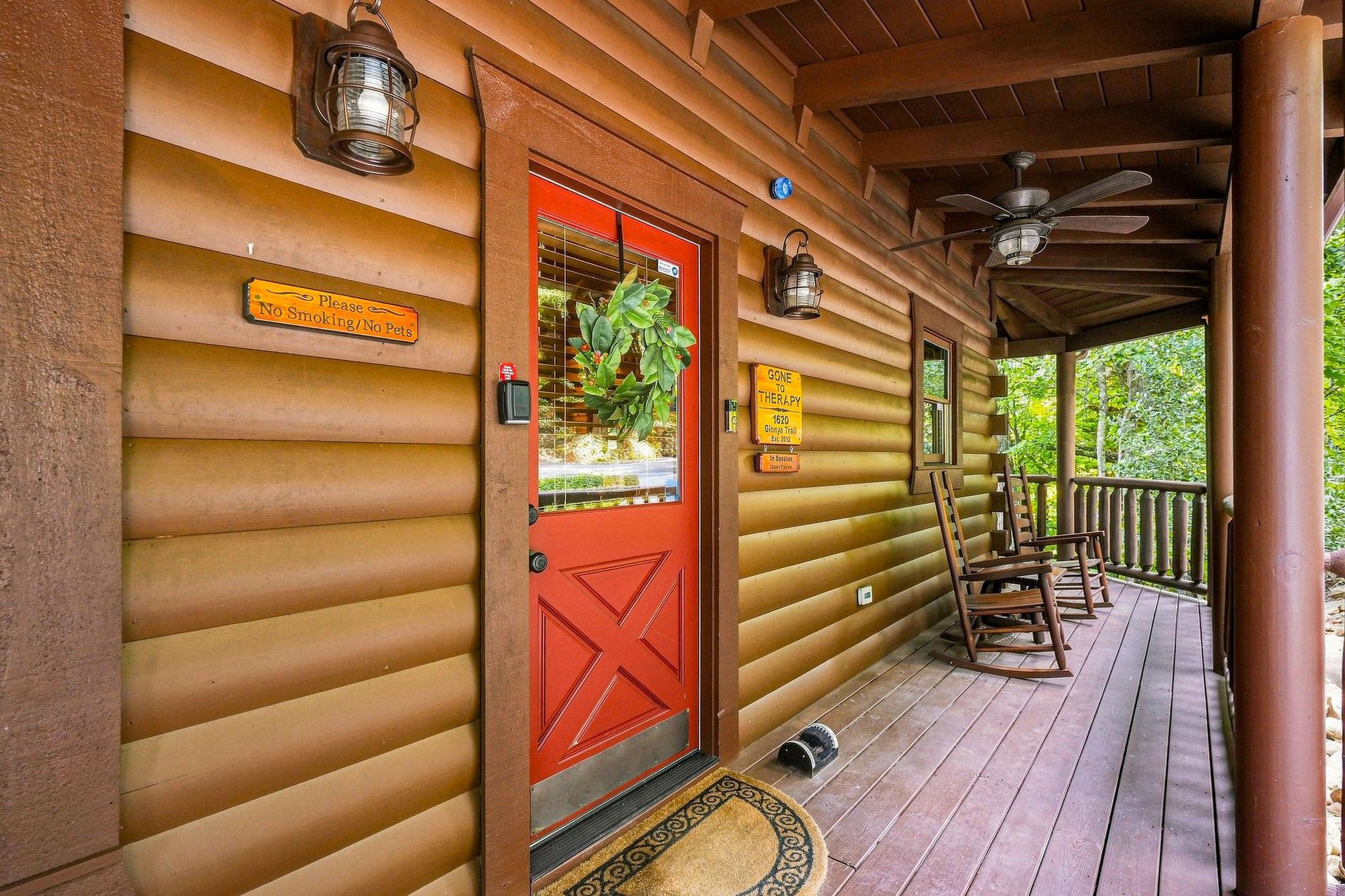 Step onto your welcoming covered porch, where rustic log siding and charming lanterns frame a cheerful red door. Settle into a rocking chair, breathe in the forest air, and let the peaceful wooded set