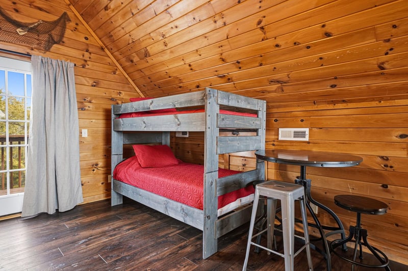 Your cozy cabin bedroom features rustic bunk beds with bright red linens, perfect for family adventures in this charming woodlined retreat.