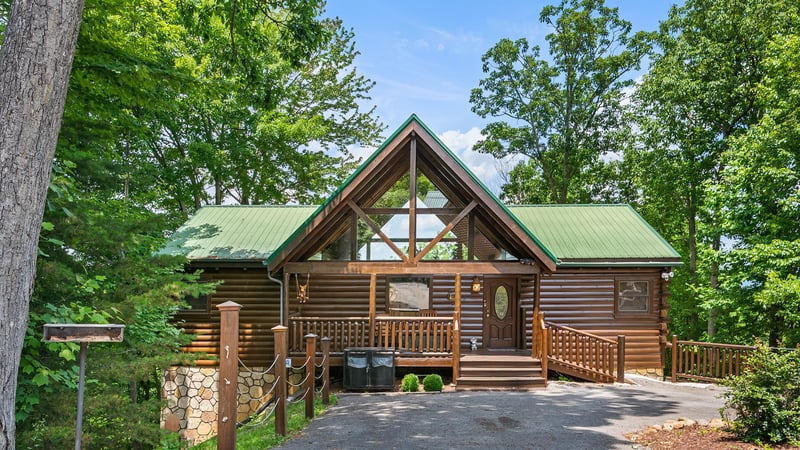 A beautiful log cabin retreat nestled among towering trees, featuring a charming green metal roof and welcoming covered porch perfect for mountain getaways.
