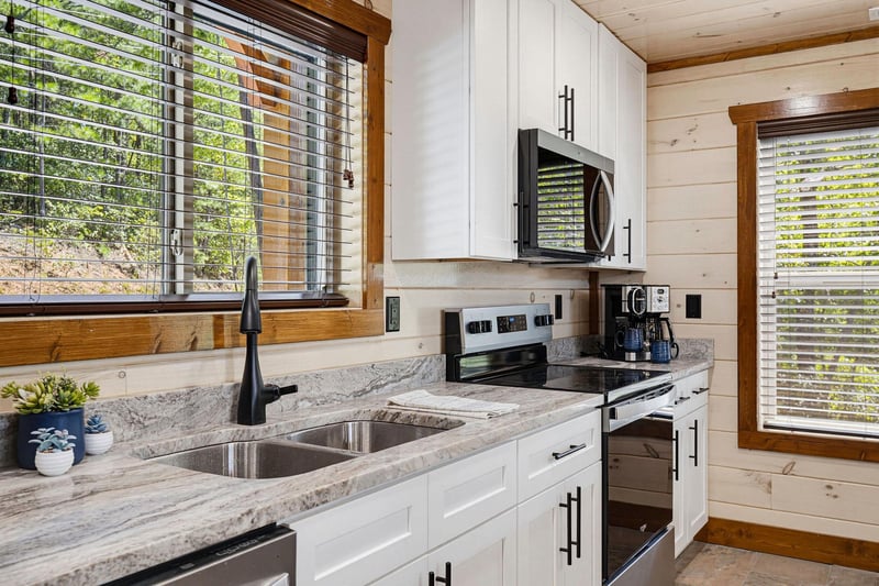 Prepare your favorite meals in this bright, fully equipped kitchen with modern appliances, granite countertops, and plenty of natural light streaming through woodenframed windows overlooking the surr