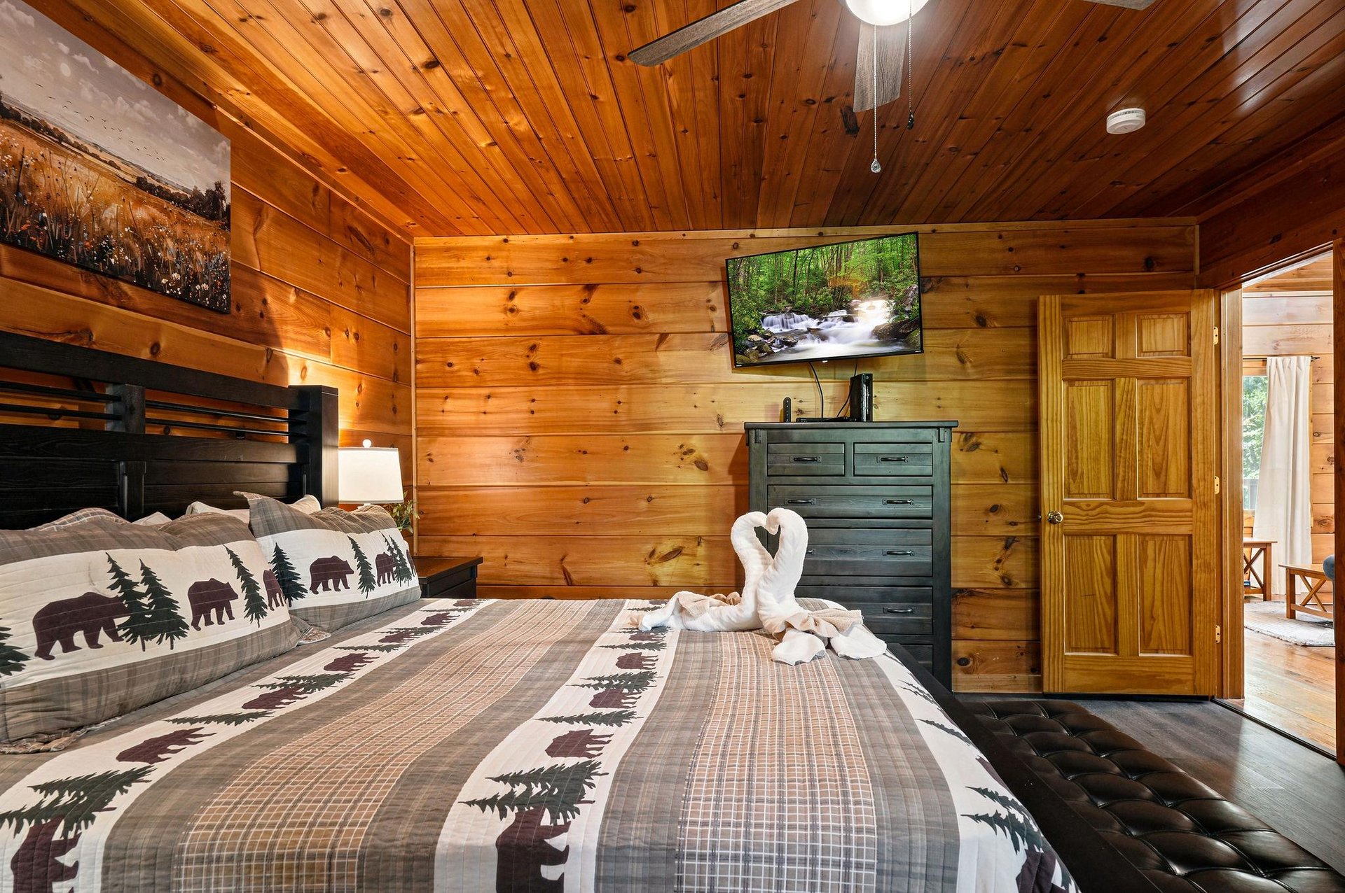 Cozy cabin bedroom with vaulted wood ceilings, rustic bearthemed bedding, flatscreen TV, and charming towel swans awaiting your mountain getaway.