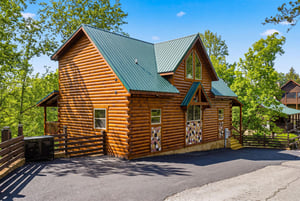 Beautiful log cabin nestled among towering trees with spacious parking and charming rustic details.