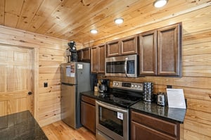 Your fully equipped kitchen features rich wood cabinets, granite counters, and modern appliances in a cozy log cabin setting.