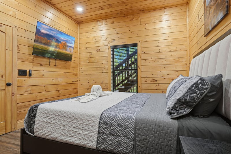 Unwind in your cozy cabin bedroom with warm wood walls, a comfy bed, and modern TV for perfect relaxation after mountain adventures.