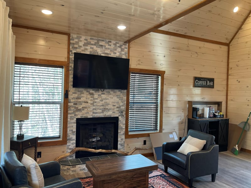 Cozy up in your rustic living room with exposed wood beams, stone fireplace, and modern TV for perfect mountain cabin evenings.