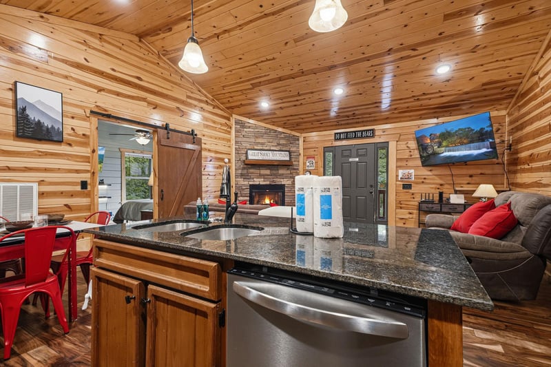 Warm wood envelops your open living space, where a granitetopped kitchen island flows naturally into a cozy fireside lounge. Rustic barn doors and cheerful red accents bring charm to your mountain re