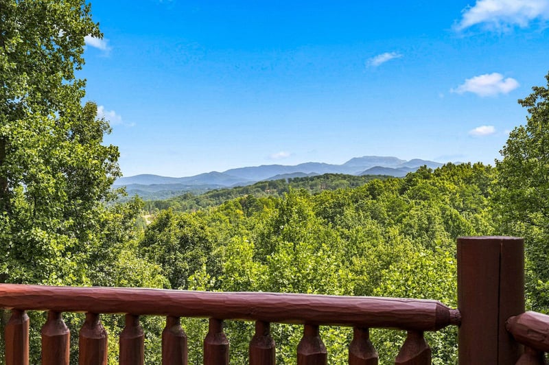 Stunning mountain vistas stretch across the horizon from your private deck, framed by lush forest canopy and clear blue skies.