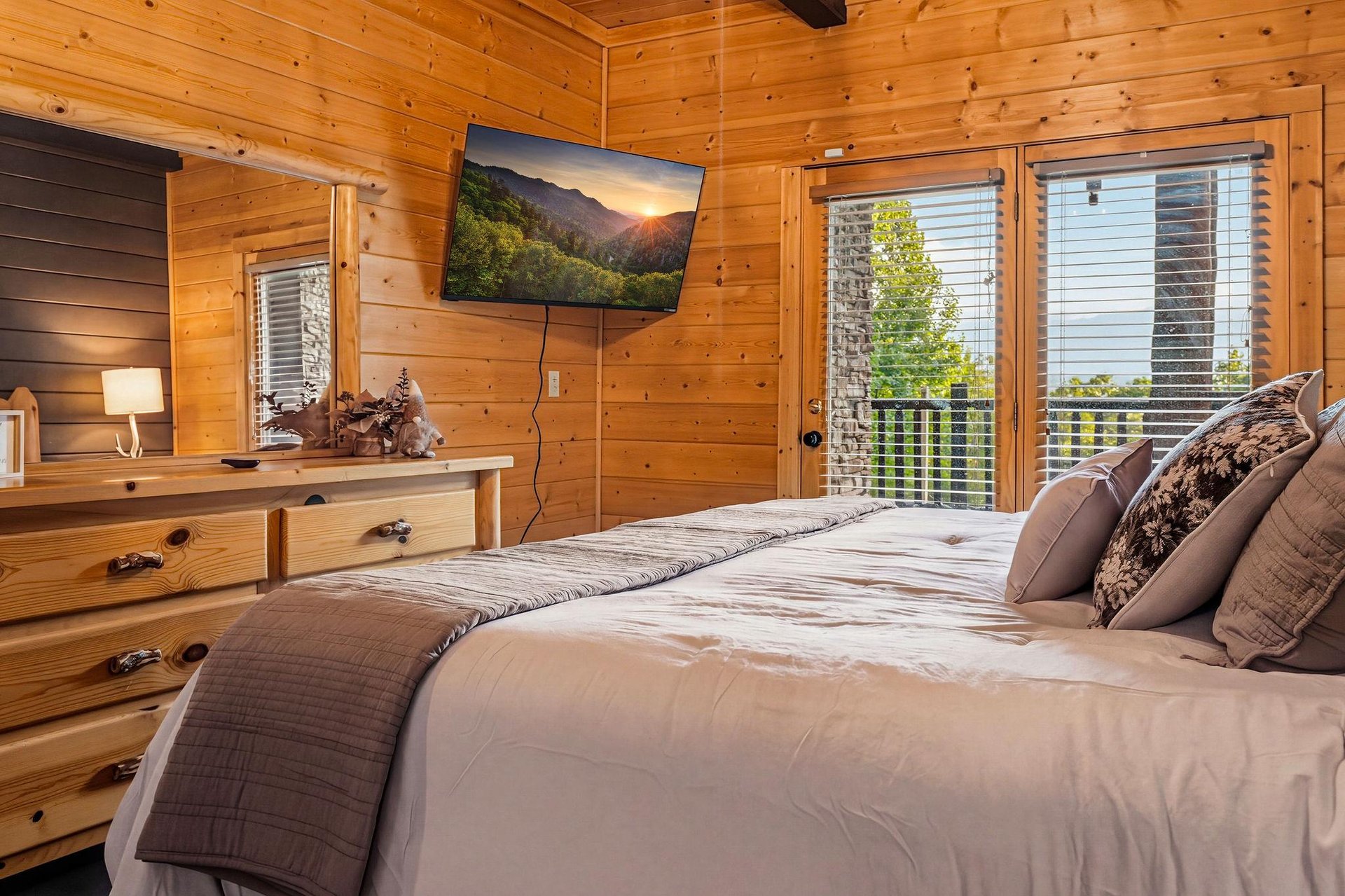 Step into your cozy mountain retreat with warm wood walls and a plush bed. Natural light fills the room from the balcony, where peaceful green views await.