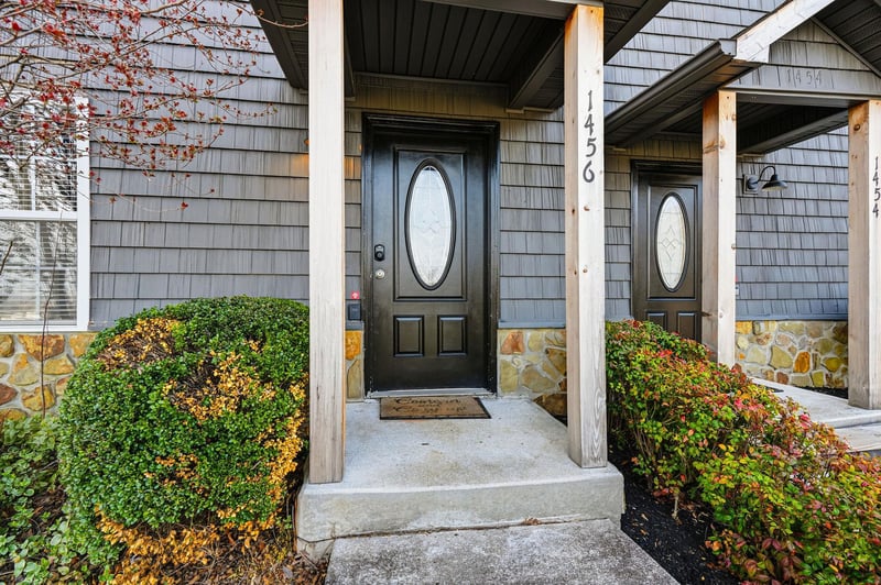 Modern property entrance showcases attractive architecture with covered porch, decorative glass door, and beautifully landscaped seasonal foliage.