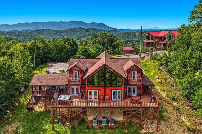 A striking red mountain lodge nestled among forested peaks offers sweeping panoramic views. The spacious wraparound deck and elevated design create a secluded retreat surrounded by natural beauty.