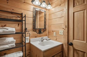 Step into your cozy log cabin bathroom, where warm wood surrounds you and fluffy towels await on rustic shelving.