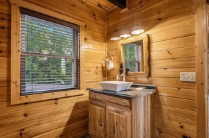 Natural light streams through the window onto warm wood plank walls and a rustic vanity with vessel sink, creating your own cozy cabin retreat.