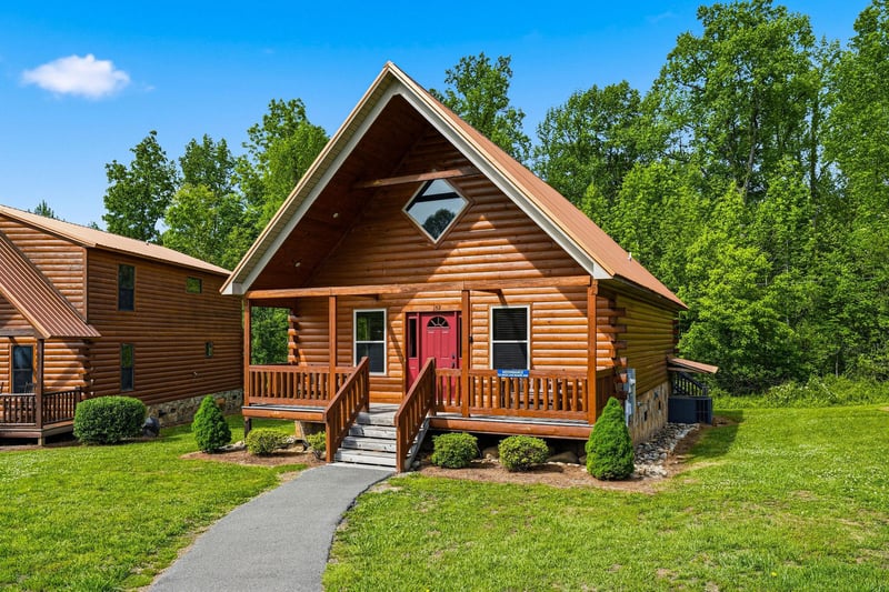 Charming log cabin exterior with a welcoming red door, covered porch, and lush green surroundings perfect for your mountain retreat.