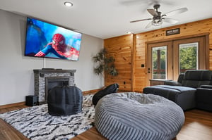 Relax in your private movie lounge with cozy seating and a fireplace, opening to natural light and views of the surrounding greenery.
