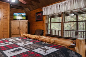 Relax in this cozy cabinstyle bedroom with rustic wood details and a handcrafted log bed frame. The vaulted ceiling adds warmth, while the TV and natural light make your retreat both comfortable and 