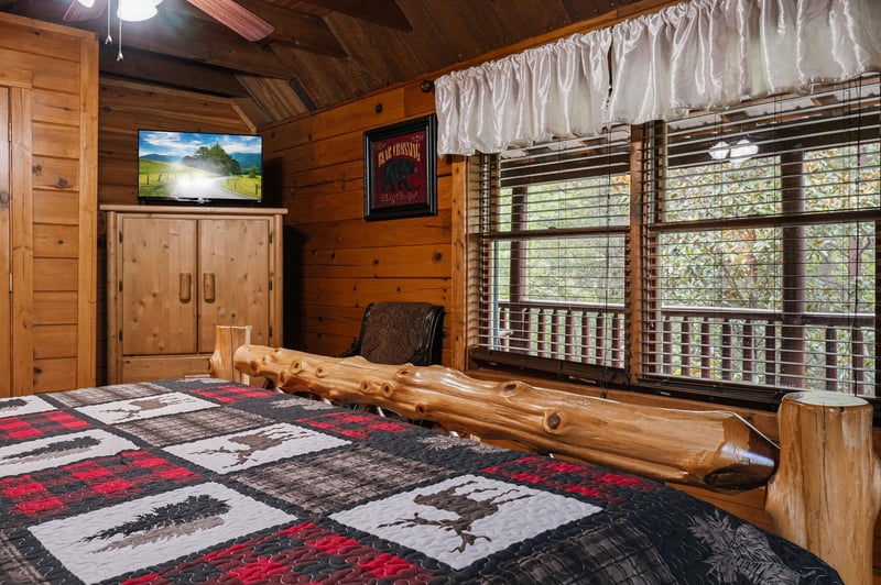 Relax in this cozy cabinstyle bedroom with rustic wood details and a handcrafted log bed frame. The vaulted ceiling adds warmth, while the TV and natural light make your retreat both comfortable and 