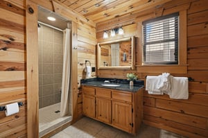 Unwind in your rustic cabin bathroom, where warm wood surrounds granite counters and a spacious tiled shower awaits your refreshing retreat.