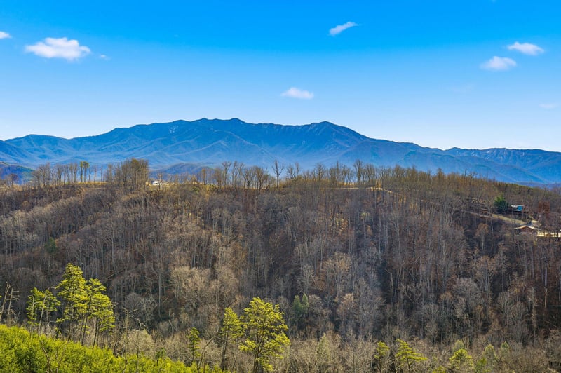 Stunning mountain landscape with layered ridges and rolling forested hills stretching toward distant peaks under bright blue skies.