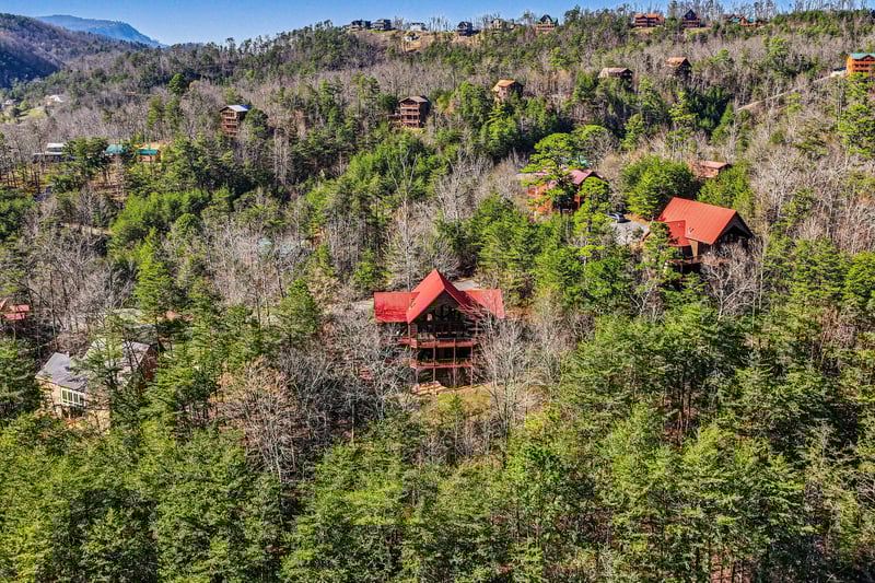 Aerial view of mountain cabins nestled among forested hills, showcasing the peaceful woodland setting of this vacation rental destination.