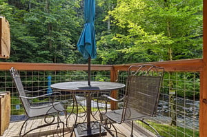 This deck overlooks lush forest and a creek, creating a serene setting for your morning coffee or evening unwind. The umbrellashaded table and mesh chairs invite you to relax outdoors.