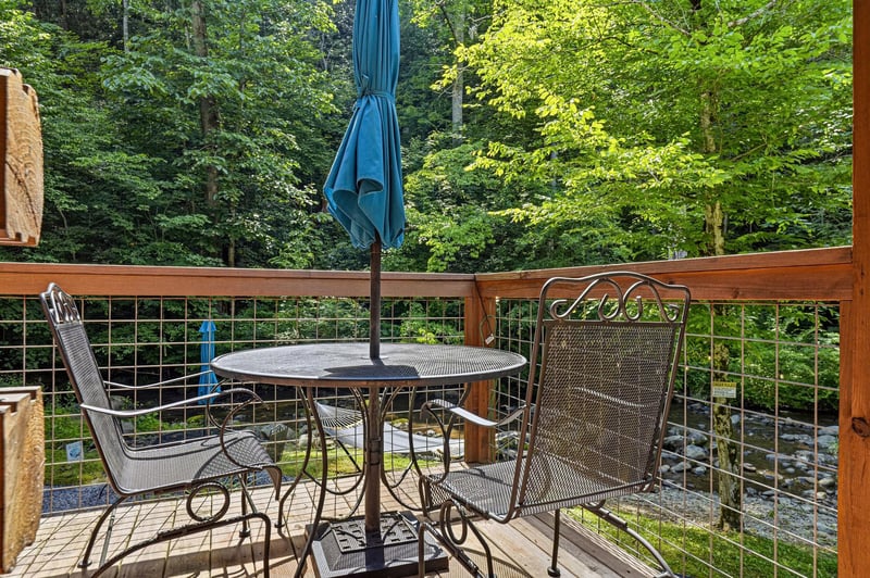 This deck overlooks lush forest and a creek, creating a serene setting for your morning coffee or evening unwind. The umbrellashaded table and mesh chairs invite you to relax outdoors.