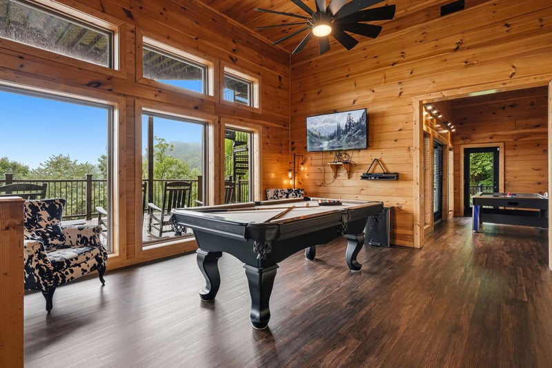 Gather around the sleek billiards table in this stunning game room, where floortoceiling windows frame breathtaking mountain views and natural light fills the warm woodpaneled space.