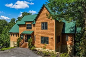 This charming cabin features warm wood siding and a distinctive green metal roof, nestled among lush trees offering privacy and natural beauty in a peaceful mountain setting.