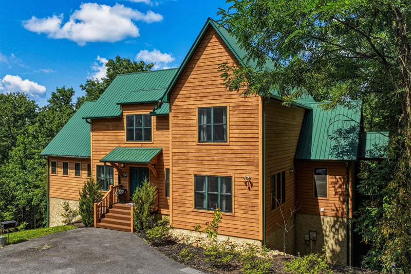 This charming cabin features warm wood siding and a distinctive green metal roof, nestled among lush trees offering privacy and natural beauty in a peaceful mountain setting.