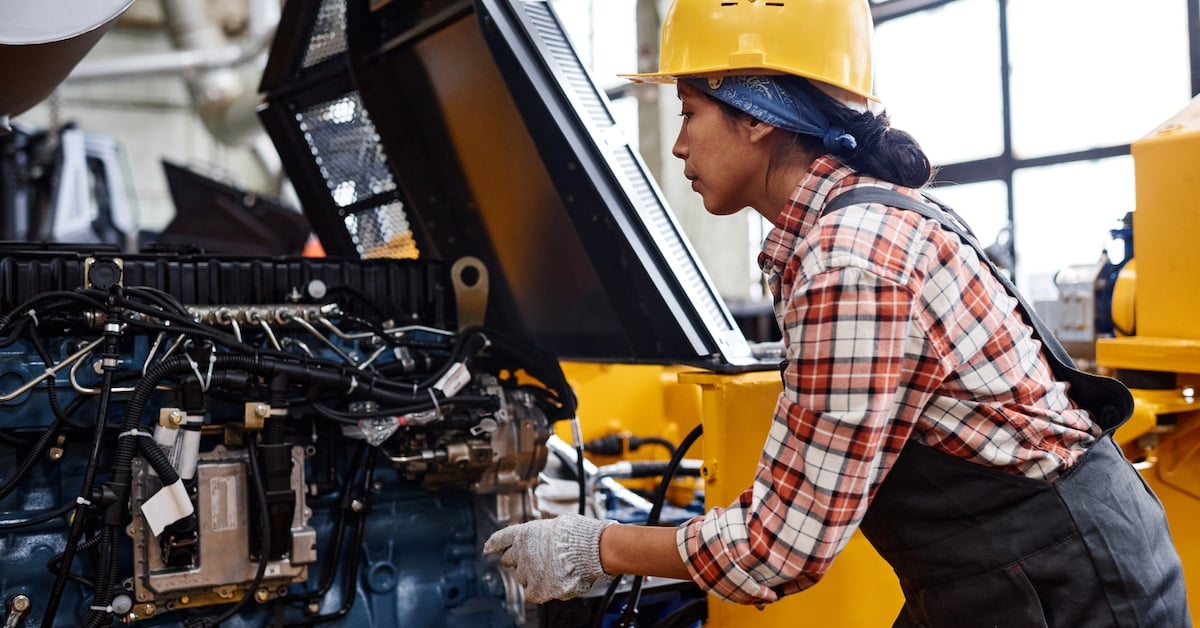 Female technician in coveralls and hardhat inspecting industrial equipment