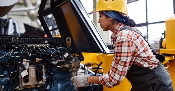 Female technician in coveralls and hardhat inspecting industrial equipment